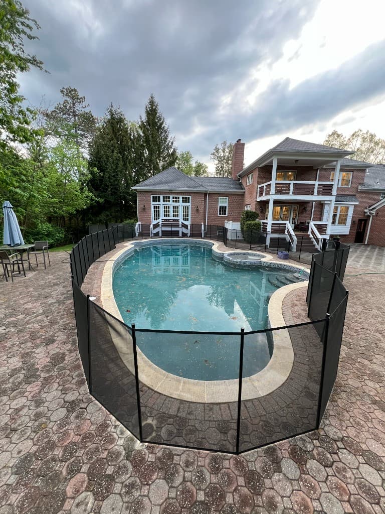 Kidney pool with cloudy water, removable mesh safety fence, and brick paver deck, typical opening or chemistry call before we vacuum, treat, and test for loss.