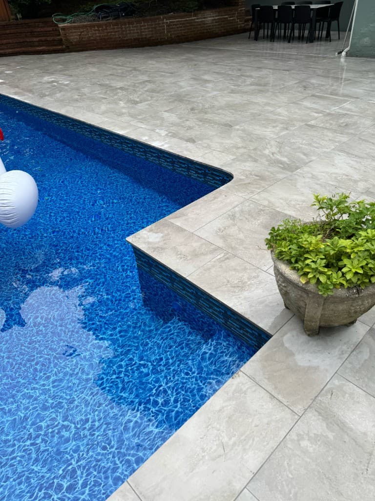Blue mosaic waterline tile with light stone coping and deck planters, finish detail after leak checks and grout or coping resets.